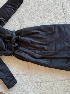 Svart morgonrock från Victoria's Secret - Lyxig svart morgonrock från Victoria's Secret i mjukt, glansigt material. Lång modell med knytskärp i midjan och långa ärmar. Perfekt för att chilla hemma i stil. Klassisk och elegant design med en skön känsla mot huden.