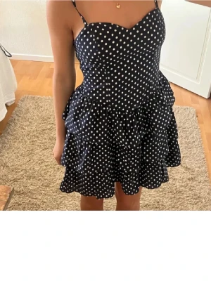 Mörkblå prickig volangklänning - Supersöt mörkblå kortklänning med vita prickar och volangkjol. Klänningen har hjärtformad urringning och kan bäras både med och utan axelband. Perfekt för sommarens alla tillfällen!