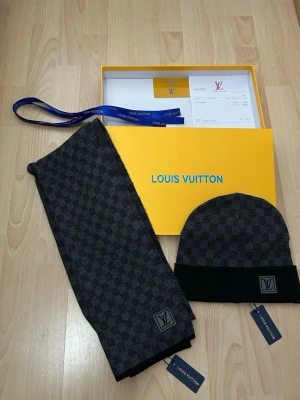Lv svart set - Säljer en grå och svart mössa och halsduk från Louis Vuitton med klassiskt rutigt mönster och diskret LV-logga framtill. De har en stilren look och är tillverkad i ett mjukt material som känns lyxigt. Perfekt för dig som vill ha något exklusivt och tidlöst.