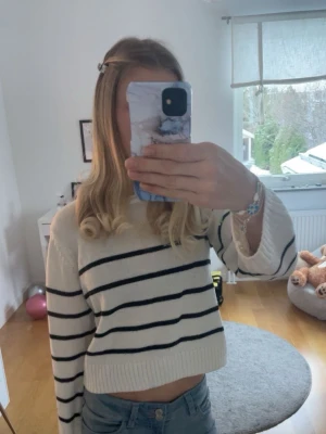 Vit stickad tröja med svarta ränder - Säljer en vit stickad tröja med svarta ränder. Tröjan har en rund halsringning och långa ärmar med ribbade muddar. Perfekt för att skapa en avslappnad och trendig look. Jag är 14 och såhär sitter tröjan på mig🤗🌸🥰🩷