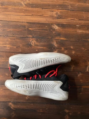 Svarta sneakers med röd snörning - Snygga sneakers i svart med vita, strukturerade sidor och röda skosnören. Skorna har en futuristisk design med mönstrad sula och hög komfort. Materialet är en mix av textil och syntet. Perfekta för dig som vill sticka ut med din stil.