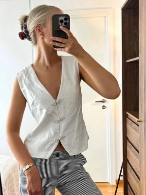 Vit linnetopp med knytknappar - Säljer min så fina väst som INTE går att få tag på längre! I vitt linne med djup v-ringning och dekorativa knappar framtill. Strlk 34 och från NA-KD.