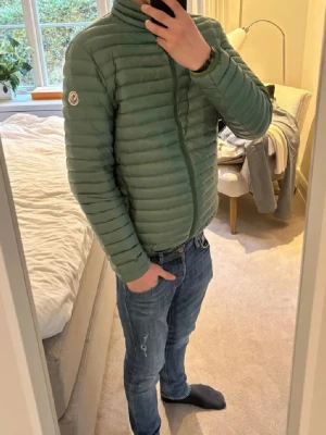 Moncler Jacka - Säljer en stilren grön pufferjacka från Moncler med diskret logga på ärmen och dragkedja framtill.                                                                                                                         Bra skick ✅.                                                                                      Storlek: M                                                                                      Skriv om ni har frågor 🙌 (Jag e rätt så kort därav att den e förstor)