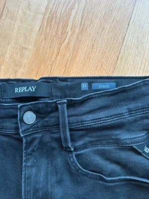 Svarta Replay Anbass jeans - Snygga svarta jeans från Replay, modell Anbass. Klassisk femficksdesign med smal passform och detaljerade sömmar. Jeansen har en diskret tvättad look och är tillverkade i stretchigt material för extra komfort. Perfekta för dig som gillar stilrena och moderna jeans. Kan tänka mig gå ner i pris vid snabb affär.