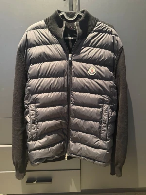 Moncler Teicot Cardigan / Hybridjacka – Svart – L - Säljer en Moncler Tricot Cardigan i svart. Dun fram och stickade ärmar/rygg – väldigt skön och perfekt som vår/höstjacka. * Kvitto finns • Storlek L • Köpt på NK 2025 • Mycket fint skick • Nypris runt 10 000 kr