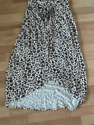 Leopardmönstrad kjol med knyt - Snygg kjol med leopardmönster i beige, brunt och svart. Kjolen har en omlott-look med knyt framtill och är tillverkad i ett mjukt och lätt tyg, perfekt för dig som vill sticka ut. Passar dig som gillar djurmönster och vill ha en kjol med cool attityd.