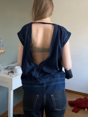 Mörkblå topp med öppen rygg - Snygg mörkblå topp med cool öppen rygg och dekorativa sömmar längs ärmar och nederkant. Modellen är ärmlös och har en avslappnad passform