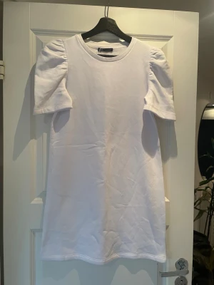 Vit klänning  med puffärm från zara - Säljer en vit klänning från Zara med trendiga puffärmar. T-shirten har rund halsringning och är gjord i mjuk bomull. Perfekt för dig som vill ha en basic med en twist i garderoben.