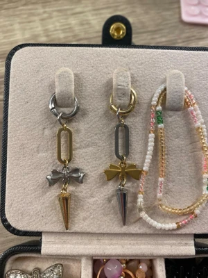 Asymmetriska örhängen med rosetter - Unika örhängen i mixade metaller med geometriska former och små rosetter. Ena örhänget har en silverfärgad rosett och guldfärgad kon, det andra har en guldfärgad rosett och silverfärgad kon. Säljs som ett par. De är gjorda i rostfritt stål och köpta för 200kr, typ helt oandvända 