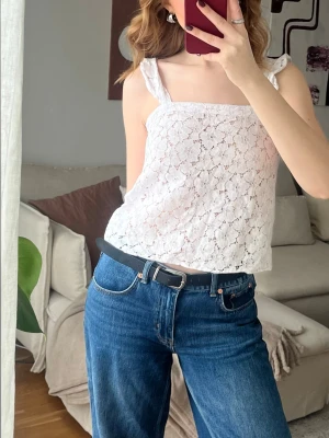 Vit spetstopp med breda axelband - Säljer en vit linnetopp med breda axelband och vacker spetsdetalj. Toppen är ärmlös och har ett blommigt spetsmönster som ger en romantisk vibe. Perfekt för sommarens varma dagar och lätt att matcha med jeans eller kjol.