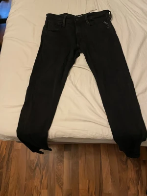 Svarta replay slim fit  - Säljer ett par svarta slim fit jeans från Jack & Jones. Klassisk femficksmodell med dragkedja och knapp i midjan. Jeansen har en stilren look och är tillverkade i stretchigt material för extra komfort.