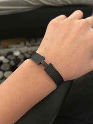Svart armband med H-detalj - Snyggt svart armband i metall med en stilren H-formad detalj framtill. Armbandet har en modern och minimalistisk design som passar perfekt till en trendig look. Lätt att matcha med andra accessoarer och ger en cool touch till outfiten.