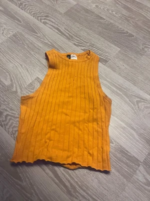 Ribbad orange linnetopp från H&M - Snygg ribbad linnetopp i en stark orange färg från H&M Divided. Toppen är ärmlös med rund halsringning och har en croppad passform. Perfekt att styla med jeans eller kjol för en trendig look.