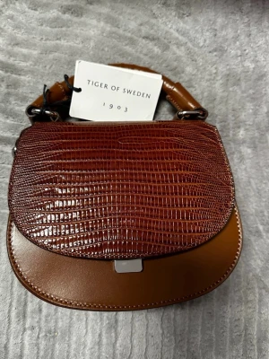 Tiger Of Sweden Handbag - The handbag is brand new, never use. Shoulder bag from Tiger of Sweden Adjustable shoulder strap Lid with magnetic button closure Two inner compartments, one with zipper Embossed logo at front Dust bag included