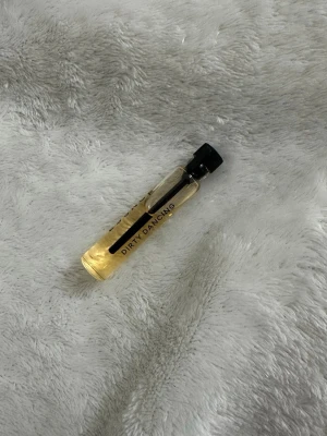 Dirty Dancing parfymprov - Litet parfymprov med texten Dirty Dancing på glasflaskan. Flaskan är genomskinlig med svart lock och innehåller en ljusgul vätska. Perfekt att ha med i väskan eller testa en ny doft.