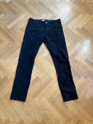 Svarta kostymbyxor från Filippa K - Stilrena svarta kostymbyxor från Filippa K med klassisk rak passform. Byxorna har knapp och dragkedja framtill samt diskreta fickor. Perfekta för en clean och dressad look. Materialet känns mjukt och följsamt.