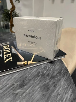 Byredo Bibliothèque Eau de Parfum - Byredo Bibliothèque Eau de Parfum i elegant vit kartong med subtilt mönster. Doften är känd för sina lyxiga och unika noter, och förpackningen har en stilren och minimalistisk design. Perfekt för dig som gillar exklusiva parfymer.