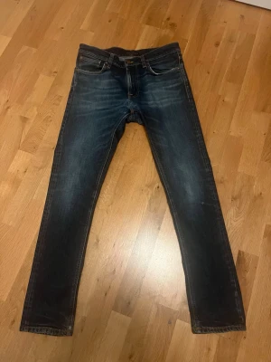 Nudie lean Dean - Säljer ett par mörkblå slim fit jeans från Nudie med riktigt bra slitingar storleken är 32-32 och måtten kan kan jag skicka vid funderingar skada i skrevet som är lagad av nudie riktigt diskret så inget som pajar helhetsintrycket 