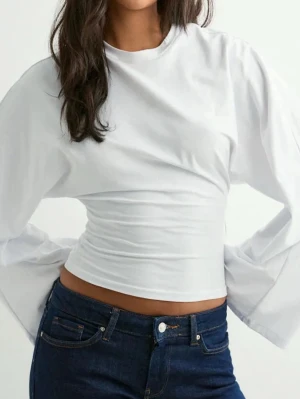 Vit croppad långärmad topp - Trendig vit croppad topp med långa ärmar och rund hals. Toppen har en slim passform perfekt för en clean och stilren look. Enkel att matcha med både jeans och kjol. Använd endast 1 gång