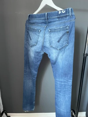 Blå Dondup george  - Snygga blå slim fit jeans från Dondup med slitningar och en liten reva på vänster lår. Jeansen har klassiska fem fickor, dragkedja och knapp i midjan samt diskreta detaljer på bakfickorna. Perfekta för en avslappnad och trendig look.