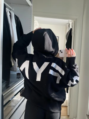 Svart hoodie från DFYNE med tryck - Cool svart hoodie från DFYNE med stor vit logga på ryggen och vita detaljer på ärmarna. Klassisk huva med dragsko och stor magficka framtill. Perfekt för en avslappnad streetwear-look.