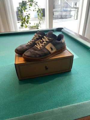Blå Polo Ralph Lauren sneakers - Snygga sneakers från Polo Ralph Lauren i blå mocka med beige detaljer och klassisk logga på sidan. Dom är ganska slitna därför det låga priset men skorna ser ändå bra ut och passar till mycket. 