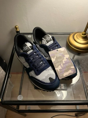 Valentino Garavani blåvita sneakers - Snygga sneakers från Valentino Garavani i marinblått och vitt med meshpaneler och mockadetaljer. Skorna har klassisk låg siluett, vita och blå skosnören samt märkets logga på plösen. Original spris 7000kr!