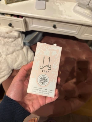 Yara Eau de Parfum 50ml - Säljer en parfym från Yara, Eau de Parfum i en elegant ljusrosa kartong med vita blommönster och silverdetaljer. Flaskan rymmer 50 ml och har 80% volym. Perfekt för dig som gillar stilrena och feminina dofter.