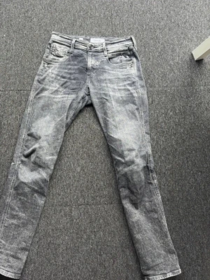 Replay Anbass grå slim jeans - Snygga grå jeans från Replay, modell Anbass med slim fit passform. Jeansen har klassisk femficksdesign, dragkedjegylf och coolt tvättad look. Perfekta för dig som gillar en modern och stilren stil.