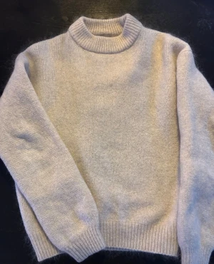 Beige stickad tröja Lindex - Mysig stickad tröja från Lindex. Tröjan har en enkel och stilren design med ribbade muddar vid ärmslut och nederkant. Perfekt för kalla dagar och enkel att matcha med olika outfits.