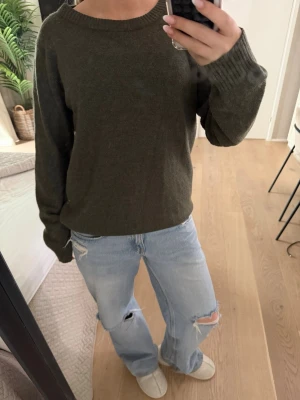 Olivgrön stickad tröja från Vila - En enkel och snygg olivgrön stickad tröja från Vila med rund halsringning och långa ärmar. Tröjan har ribbstickade muddar vid ärmslut och nederkant. Perfekt att matcha med jeans för en avslappnad look.