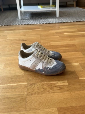 Maison margiela gats - FAST PRIS Köpta här på plick med kvitto från nk, antar då att de är äkta, därav priset.Snygga sneakers från maiden margiela i vit och grå färg med klassisk låg profil och perforerade detaljer på sidorna. Skorna har en robust gummisula och är tillverkade i läder och mocka. Perfekt för dig som gillar stilrena och trendiga skor.