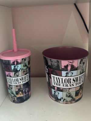 Taylor Swift The Eras Tour muggar - Säljer två muggar från Taylor Swift The Eras Tour, en med sugrör och en större utan lock. Båda har färgglada collage med bilder på Taylor Swift och texten 'The Eras Tour'. Muggarna är i plast med rosa detaljer och passar perfekt för fans.