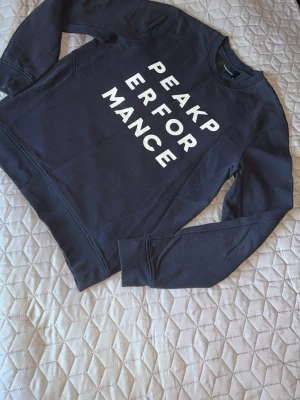 Svart sweatshirt från Peak Performance - Svart sweatshirt från Peak Performance med vit text framtill. Tröjan har rund halsringning och långa ärmar. Perfekt för en avslappnad och sportig stil. Storlek M