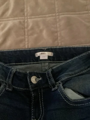 Mörkblå bootcut jeans från Gina Tricot - Säljer ett par mörkblå bootcut jeans från Gina Tricot med kontrastsömmar och snygga detaljer på bakfickorna. Jag har storlek 152 på jeans så en affär har gjort dem kortare till storlek 152 men midjan är stor så skulle rekommendera ett bälte till den