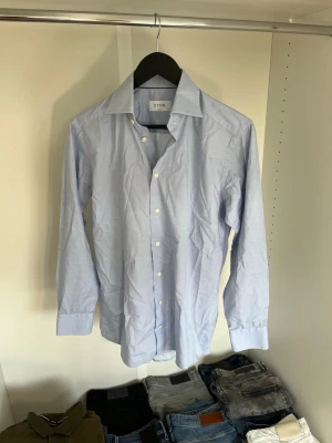 Ljusblå skjorta från Eton - Klassisk ljusblå skjorta från Eton med normal passform och långa ärmar. Skjortan har knappar framtill och är tillverkad i bomull. Hör gärna av dig vid frågor!