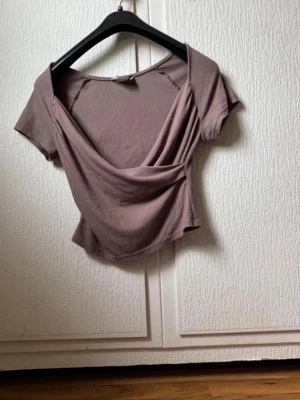 Ljusbrun omlottopp med kort ärm - Trendig ljusbrun omlottopp med korta ärmar och djup v-ringning. Toppen är ribbad och har en croppad passform som framhäver midjan. Perfekt att styla med jeans eller kjol för en snygg look.