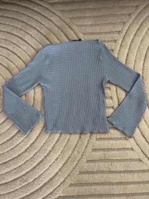 Ljusblå ribbad långärmad topp - Trendig ljusblå topp med ribbad struktur och långa ärmar. Modellen är croppad och har en lätt vågig kant vid ärmslut och nederkant. Perfekt att matcha med höga jeans eller kjol för en cool vardagslook.