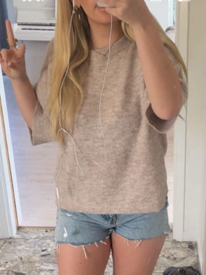 Beige stickad topp med kort ärm - Mysig beige stickad topp med rund hals och korta ärmar. Perfekt till jeans eller shorts för en avslappnad look. Materialet känns mjukt och toppen har en loose passform som ger en chill vibe.
