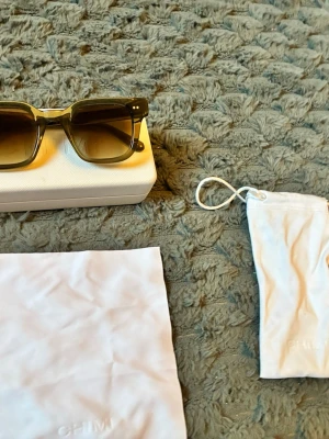 Svarta CHIM solglasögon i retrostil - Snygga solglasögon från CHIM med rektangulära svarta bågar i plast och mörka tonade glas. Kommer med vit hård förvaringsbox och tillhörande tygpåse. Perfekt accessoar för att lyfta din stil.