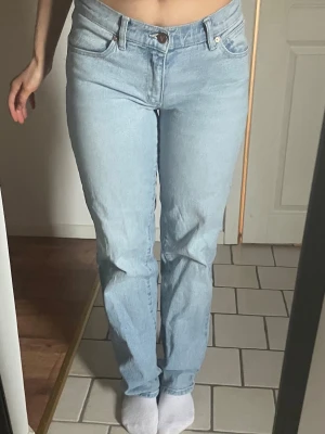 Ljusblå jeans med låg midja - Säljer ett par ljusblå jeans med klassisk femficksdesign och hög midja. Jeansen har raka ben och är tillverkade i denim med en lätt stretch. Perfekta för dig som gillar en enkel och clean look.