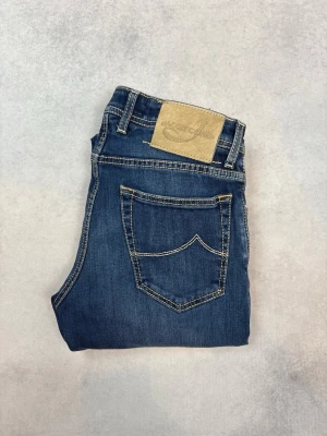 Blå jeans från Jacob cohen - Snygga blå jeans från Jacob Cohen med klassisk femficksdesign och kontrastsömmar. Jeansen har en rak passform och mellanblå tvätt med lätt slitning på låren. Perfekta för en avslappnad och trendig look.