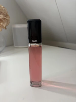 BOSS Ma Vie Eau de Parfum 75ml - BOSS Ma Vie Eau de Parfum för kvinnor i en elegant, rektangulär glasflaska med rosa doftvätska och svart lock. Förpackningen är stilren i vitt och rosa med tydlig logga. Innehåller 75 ml och har en feminin, modern design.