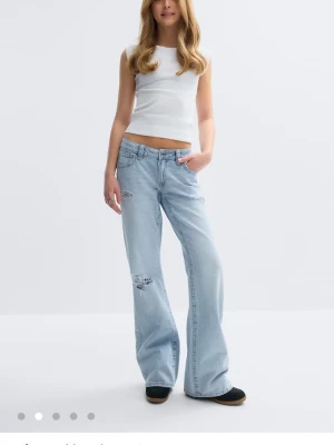 Ljusblå loose fit jeans med slitningar - Säljer ett par ljusblå loose fit jeans med låg midja och slitna detaljer på benen. Jeansen har vida ben och klassisk femficksmodell. Perfekta för en avslappnad och trendig look. Materialet är denim i bomull. dom har blitt defekter längst ned då de var för långa på mig. strl 164 i gina young