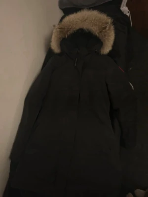 Svart parka vinter jacka från Canada Goose - Snygg svart parka vinter jacka från Canada Goose (säljer dock utan pälsen). Jackan är lång, har dragkedja framtill och klassisk röd logga på ärmen. Perfekt för kalla vinterdagar och riktigt varm. Tidlös design som funkar till allt.(äkta)