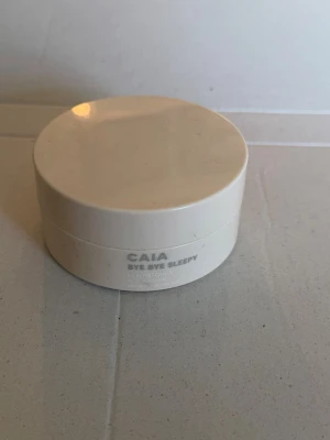 CAIA Bye Bye Sleepy Eye Patches - Fräscha ögonpatches från CAIA i en rund, beige burk. Perfekta för att pigga upp trötta ögon och ge huden under ögonen extra fukt och lyster. Patcharna är ljusrosa och har en mjuk, geléaktig konsistens.