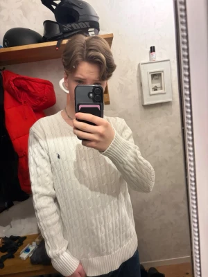 Vit kabelstickad tröja från Ralph Lauren - Vit kabelstickad tröja från Ralph Lauren med rund halsringning och den klassiska blå loggan broderad på bröstet. Tröjan har långa ärmar och ribbade muddar vid ärmslut och nederkant. Perfekt för en stilren och clean look. Tröjan är använd fåtalet gånger, inga tecken på användning. Original pris~ 2595kr. Priset är inte hugget i sten.  Skriv om ni undrar något!