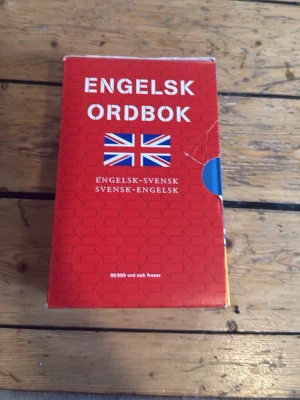 Engelsk ordbok röd - En engelsk-svensk och svensk-engelsk ordbok med röd pärm och brittisk flagga på framsidan. Boken innehåller 85 000 ord och fraser och har ett klassiskt, rektangulärt format. Perfekt för dig som vill förbättra dina språkkunskaper.