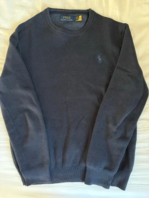 Mörkblå tröja från Polo Ralph Lauren - Klassisk mörkblå tröja från Polo Ralph Lauren med rund halsringning och diskret broderad logga på bröstet. Tröjan har ribbade muddar vid ärmslut och nederkant, och är tillverkad i ett mjukt material som passar perfekt till jeans.