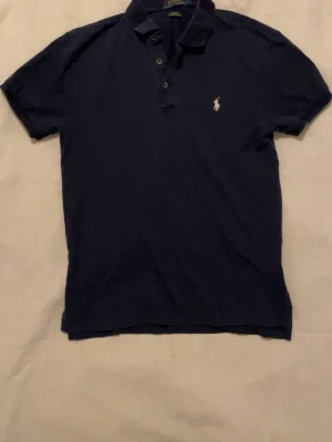 Marinblå pikétröja från Polo Ralph Lauren - Klassisk marinblå pikétröja från Polo Ralph Lauren med slim fit och stretch mesh-material. 